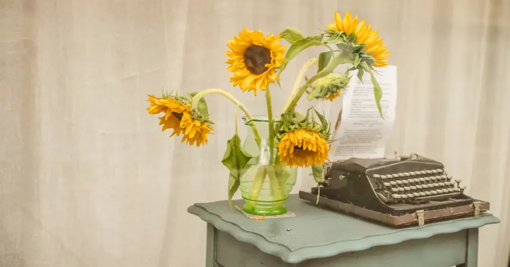 Sunflowers in a vase on a desk next to a typewriter